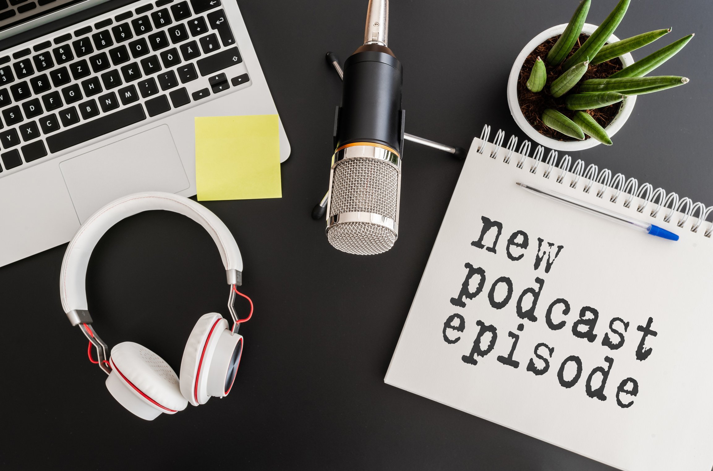 top view of podcast recording equipment on desk with words new podcast episode written on note pad